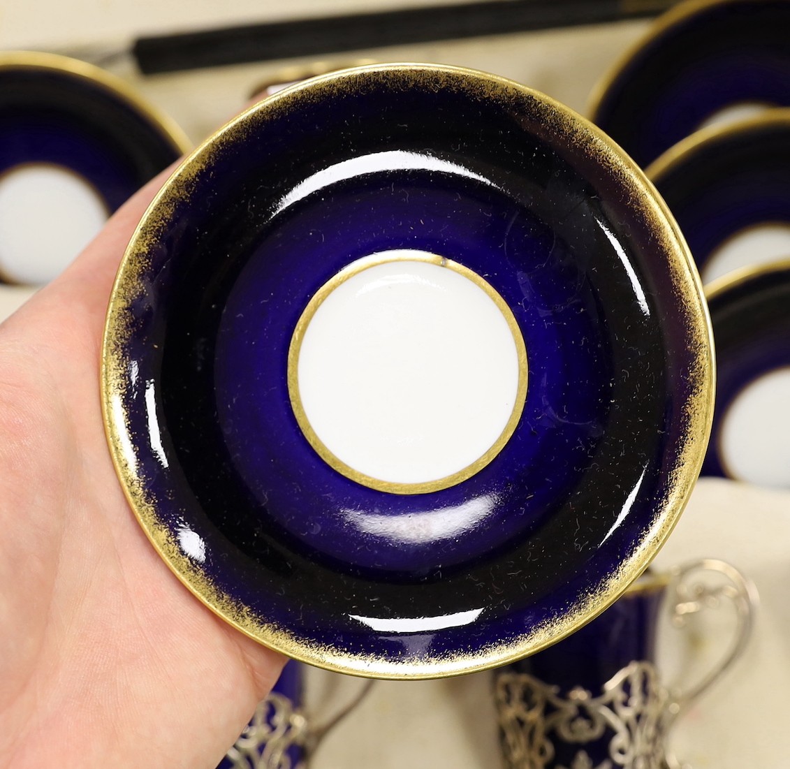 A set of six blue and gilt edged coffee cups and saucers, the cups with pierced silver holders, London, 1919, together with a set of 6 coffee spoons, triffid end terminals, Sheffield, 1925, cased